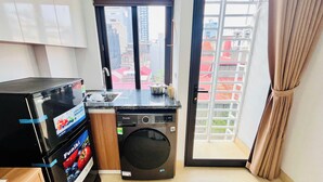 A compact kitchen with a washing machine, a small sink, and a window with a view of buildings.