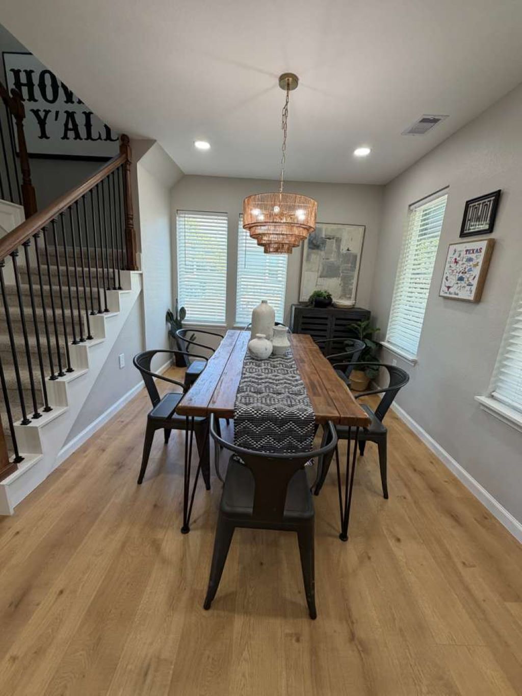 A dining area with a wooden table, black chairs, a chandelier, and a staircase with a sign.