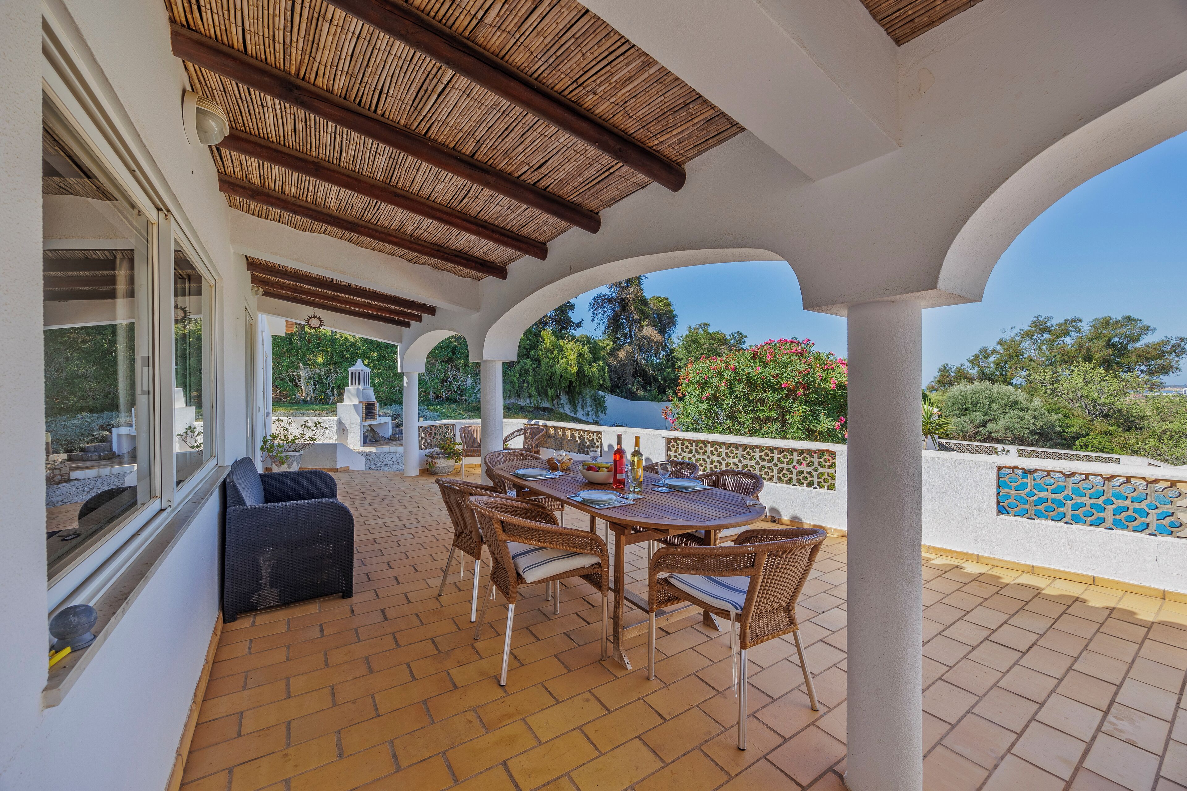Un patio cubierto con una mesa y sillas, vistas al jardín y una piscina al fondo.