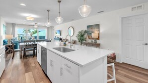 A modern kitchen with a large island, white cabinetry, and pendant lighting. - Madeira Del Mar 302 (Madeira Beach)