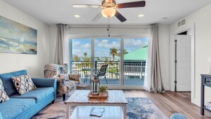 A living room with a blue sofa, a coffee table, and a ceiling fan. - Madeira Del Mar 302 (Madeira Beach)