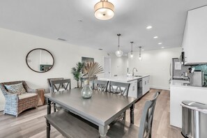 Une cuisine moderne avec des meubles blancs, un coin repas doté d’une table et de chaises en bois, et un miroir rond accroché au mur.