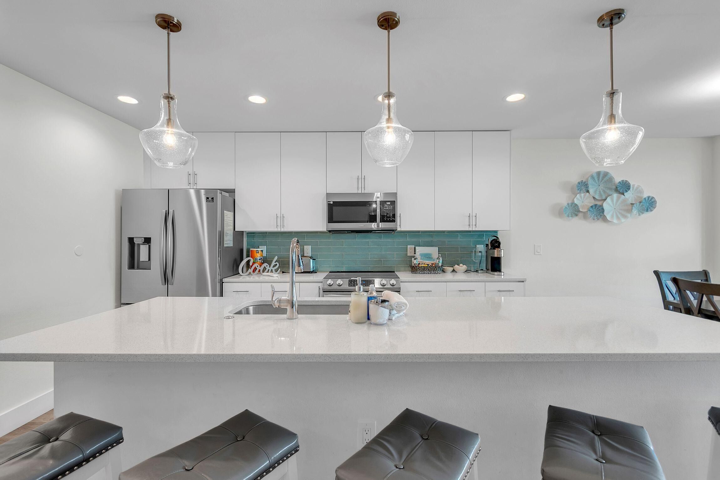 A modern kitchen with a large island, stainless steel appliances, and pendant lighting.