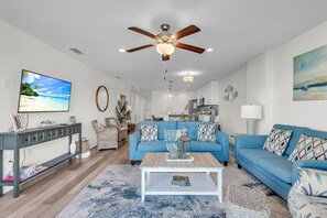 Ein Wohnzimmer mit einem blauen Sofa, einem Couchtisch, einem Deckenventilator und einem Fernseher an der Wand.