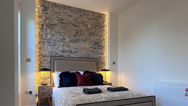 Une chambre avec un mur d’accent en pierre, un lit avec une literie à motifs, des lampes de chevet et un radiateur.