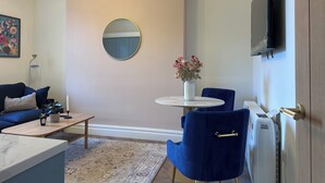 Un salon moderne avec un canapé, une table basse, un miroir rond, un vase de fleurs et un téléviseur fixé au mur.