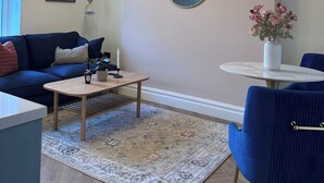 Un salon moderne avec un canapé bleu, un miroir rond, une petite table sur laquelle est posé un vase de fleurs et un luminaire décoratif au plafond.