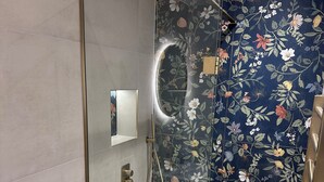 Une salle de bain moderne avec une douche à parois de verre, des toilettes blanches et un mur orné de carreaux à motifs floraux.