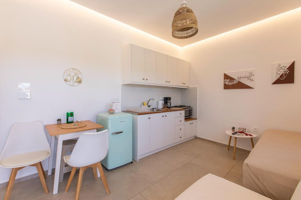 A compact kitchen with a refrigerator, microwave, and coffee maker. There is a dining area with a table and chairs, and a small seating area with a sofa.