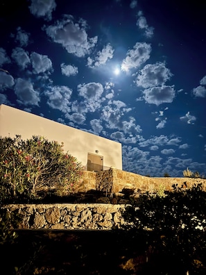 Ein Gebäude mit einer Steinwand und einer Tür, unter einem Nachthimmel mit Wolken und Mond.