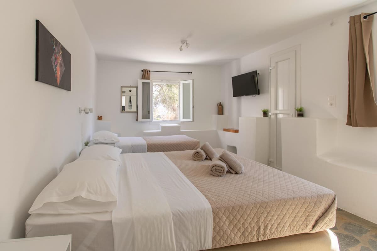 A hotel room with two beds, a TV, a window, and a bathroom visible through the door.