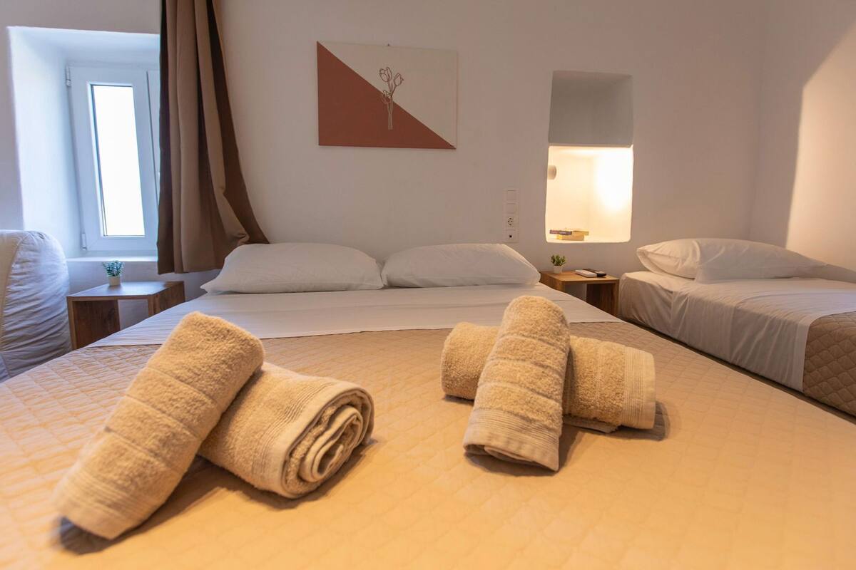 A hotel room with a bed, a bedside table, a lamp, and a window with curtains.