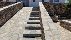 Una escalera conduce a un edificio blanco con tres puertas y ventanas, rodeado de muros de piedra.