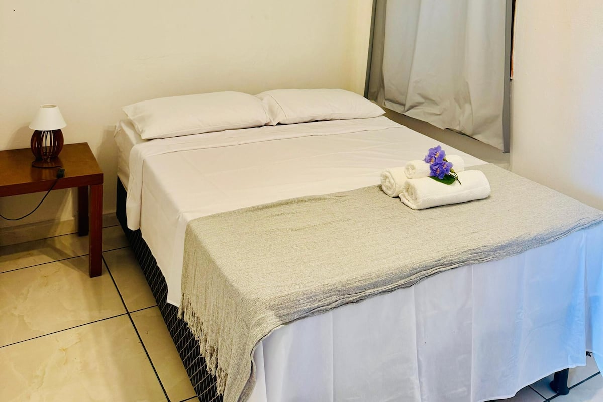 A hotel room with a bed, a nightstand with a lamp, an air conditioning unit, and a ceiling fan.