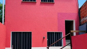 Un edificio rojo con una escalera que lleva a una puerta, una ventana y un pequeño espacio al aire libre.