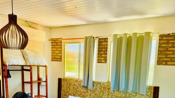 Una habitación de hotel con cama, mesita de noche, ventilador y ventana con cortinas.