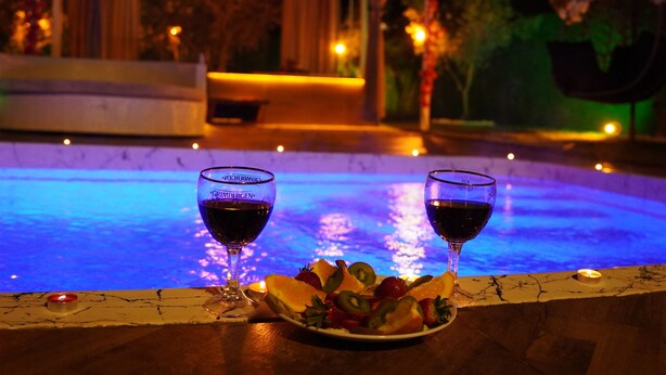 A poolside setting with two glasses of red wine, a plate of fruit, and a candle on a table. - ON2 Bungalov Villas (Dosemealti)
