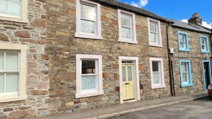 A stone building with multiple windows, a yellow door, and a red car parked outside. - Beautifully Presented Cosy Home in Kirkcudbright - Pass the Keys (Kirkcudbright)