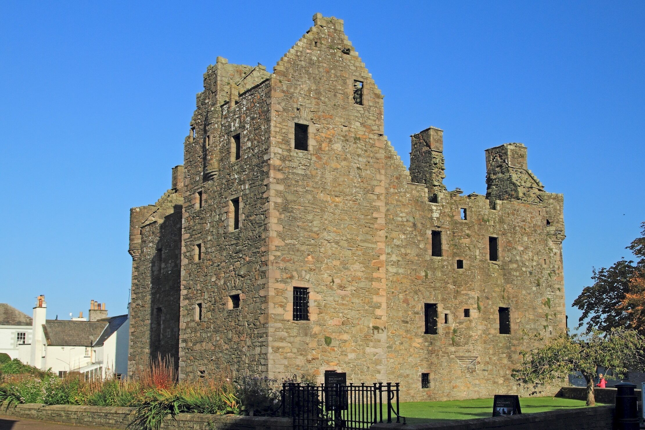 A historic stone castle with multiple towers and battlements, surrounded by a well-maintained lawn and a black iron fence.