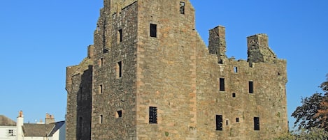 A historic stone castle with multiple towers and battlements, surrounded by a well-maintained lawn and a black iron fence.
