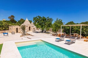 A swimming pool with lounge chairs and a pergola, surrounded by stone buildings and greenery. - Villa Trullo Desideri by Villa Plus (Casalini)