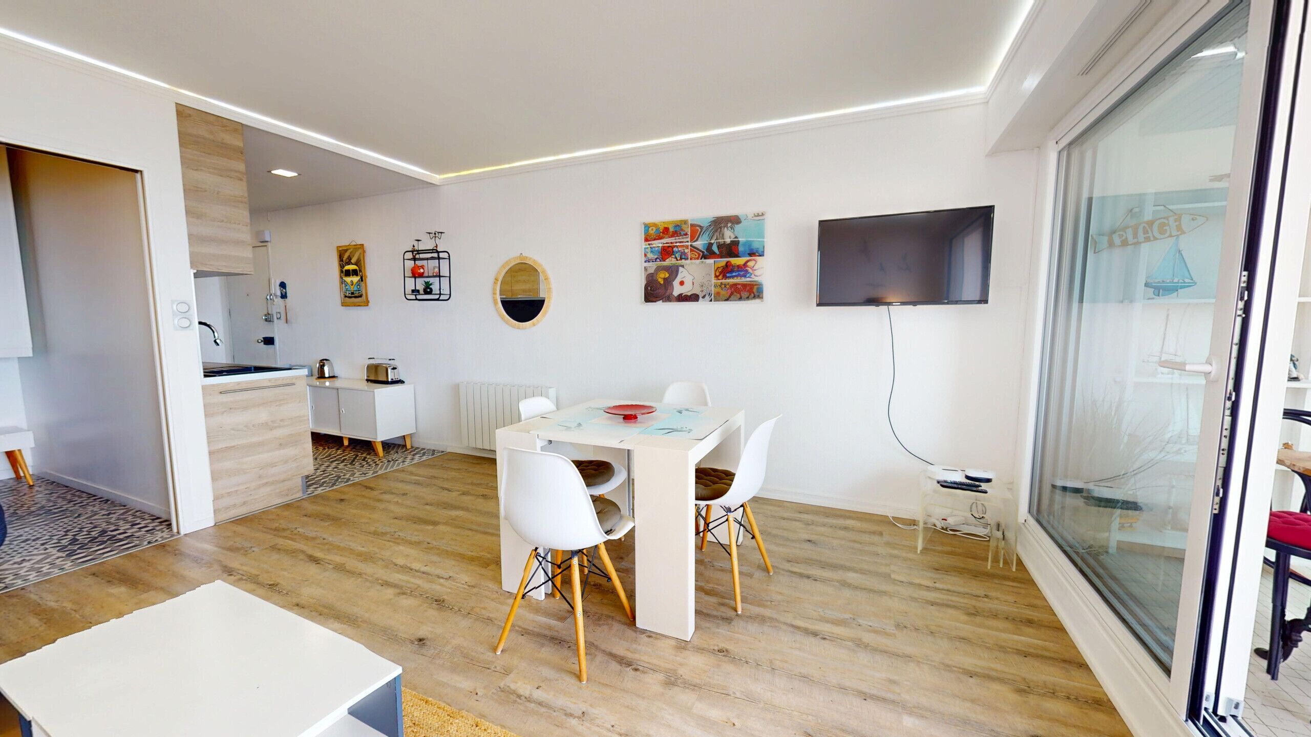 Une cuisine moderne avec des meubles blancs, un coin repas comprenant une table et des chaises blanches, et une grande fenêtre donnant sur la mer.
