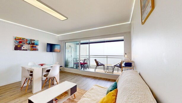 A modern living room with a sofa, a dining table, chairs, a TV, and a balcony with chairs. - Atlantide Ouest - Getaway just a stone's throw from the ocean (Saint-Hilaire-de-Riez)