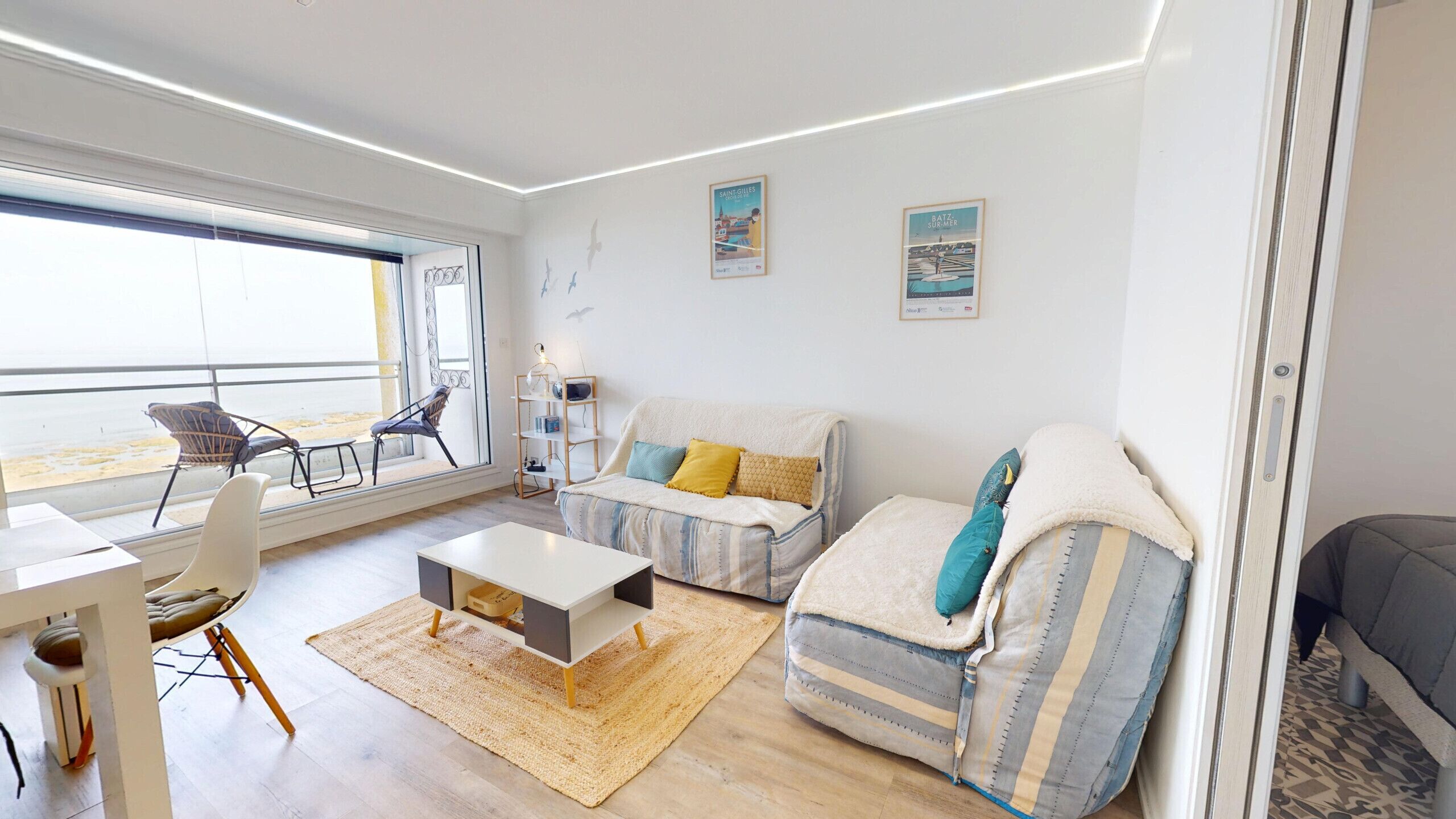 A modern living room with a sofa, armchair, and coffee table, a dining area with a table and chairs, and a large window with a view.
