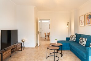 Una sala de estar con televisión, sofá, dos mesitas y un comedor al fondo.