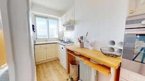 Een kleine keuken met witte kastjes, een houten aanrechtblad, een roestvrijstalen spoelbak en een inbouwoven.