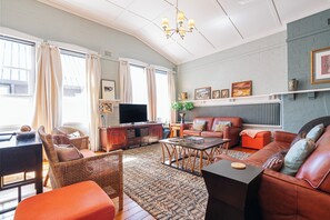 A living room with a sofa, chairs, a coffee table, a TV, and a fireplace. - Sunday School Timeless North Hobart Luxury (North Hobart)