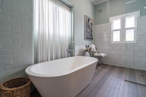 Une salle de bain avec une baignoire sur pieds, un panier en osier, un porte-serviettes et une fenêtre.