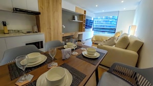 Una sala moderna con comedor, que incluye un sofá, una mesa de centro y una mesa de comedor dispuesta con platos, vasos y una copa de vino.