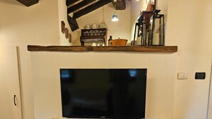 Een woonkamer met een flatscreen televisie, houten balken, een open haard en een trap.