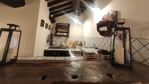 Een keuken met betegelde spatwand, houten balken, een spoelbak en verschillende keukengerei.