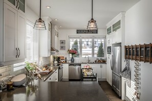 Une cuisine moderne avec des meubles blancs, des appareils en acier inoxydable et des luminaires suspendus.