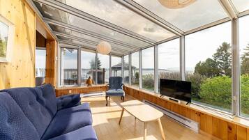 Un intérieur moderne avec un canapé, une table et un téléviseur, le tout dans une pièce dotée de grandes fenêtres offrant une vue sur l’extérieur.