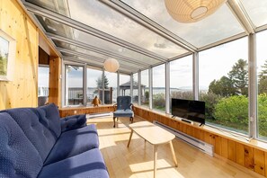 Un interior moderno con un sofá, una mesa y un televisor, todo en un ambiente con ventanas amplias que ofrecen vistas al exterior.