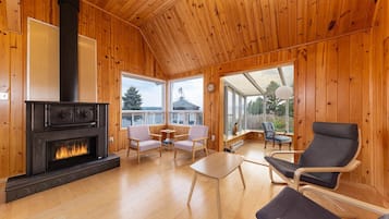 A wooden cabin interior with a fireplace, wooden furniture, and large windows.