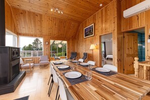 A wooden cabin interior with a dining table set for four, a fireplace, and a large window overlooking greenery. - Hôtel à la maison - Le Bleu Rivage avec spa (Saint-Joseph-de-la-Rive)