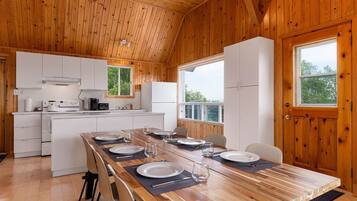 Un intérieur en bois comprenant une cuisine et un coin repas, avec une table dressée pour quatre personnes, un poêle et un réfrigérateur.