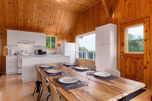 A wooden interior with a kitchen and dining area, including a table set for four, a stove, and a refrigerator.