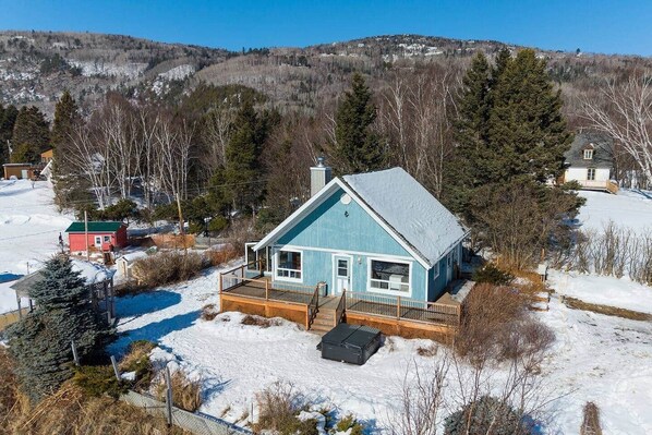 A blue house with a deck, surrounded by snow and trees. - Hôtel à la maison - Le Bleu Rivage avec spa (Saint-Joseph-de-la-Rive)