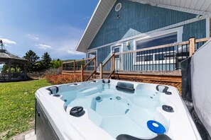 A hot tub in front of a blue house with a deck and stairs. - Hôtel à la maison - Le Bleu Rivage avec spa (Saint-Joseph-de-la-Rive)