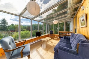 A room with a large glass wall, a wooden table, a blue sofa, and a chair.