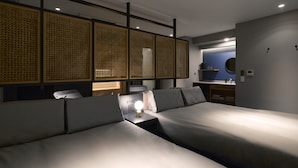 A modern hotel room with two beds, a desk, and a bathroom with a mirror and sink.