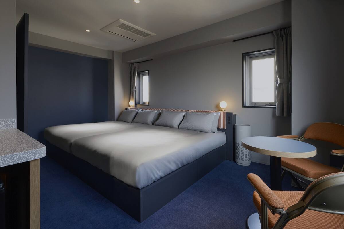 A modern hotel room with a large bed, a round table, a chair, and a window.