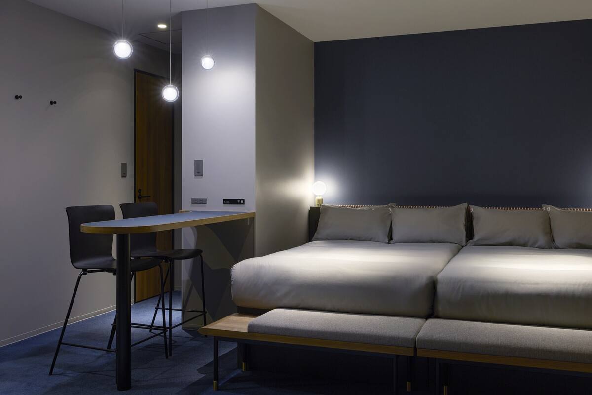 A modern room with a sofa, a small table, and two chairs. There are ceiling lights and a door in the background.