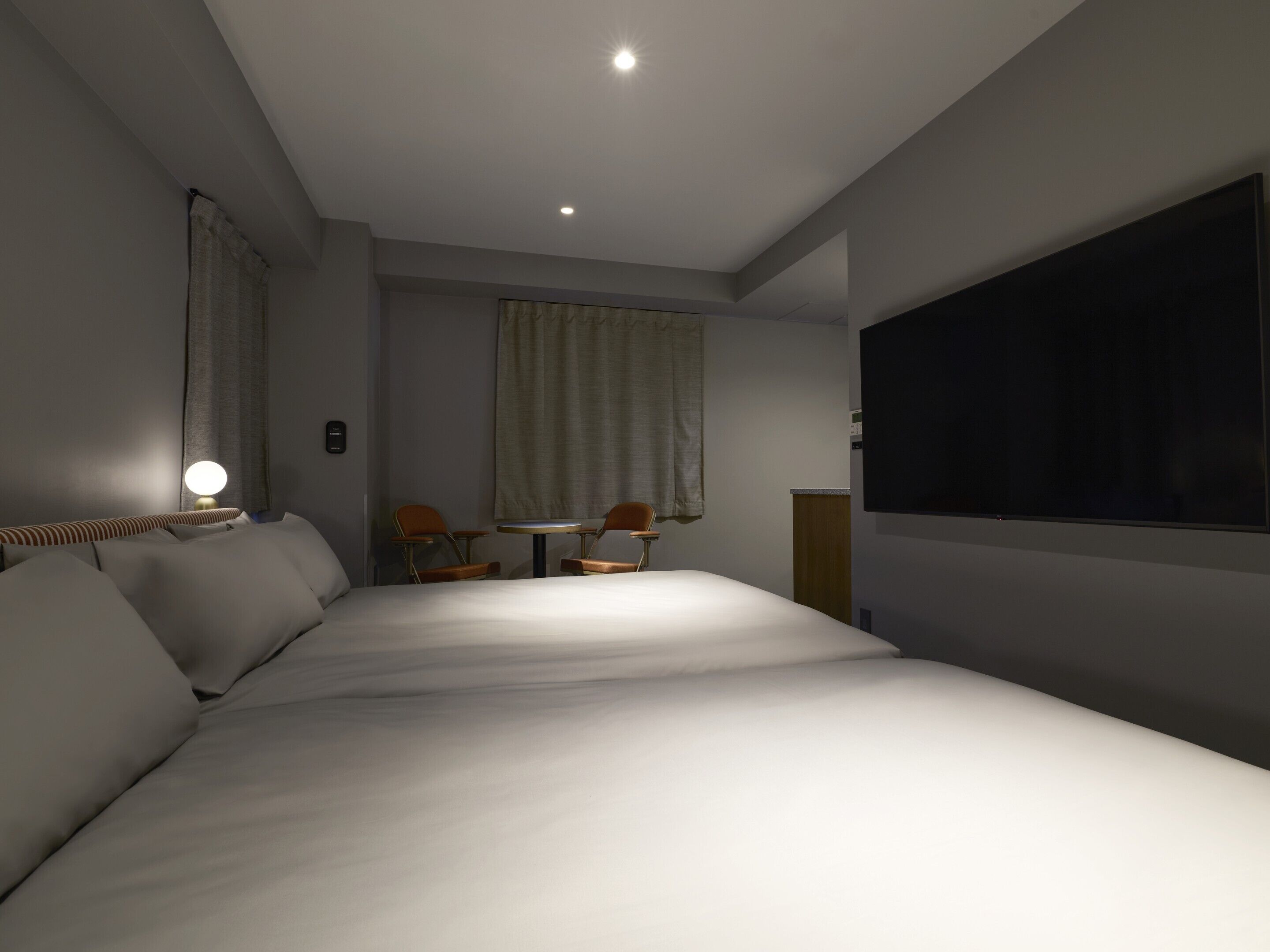 Habitación de hotel con una cama grande, un escritorio con dos sillas, un televisor de pantalla plana y un ventanal con cortinas.