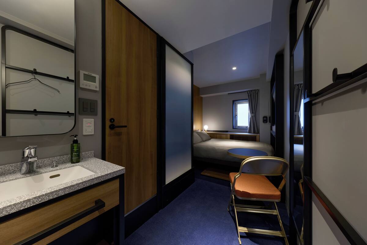A compact hotel room with a bathroom, a bed, a small table, and a chair.